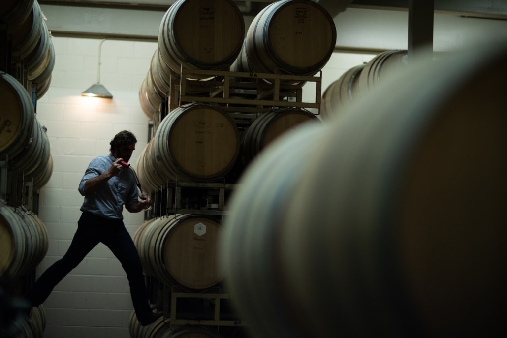 Man who works in Sonoma County wine pulling wine from a stack of barrels in a wine cellar